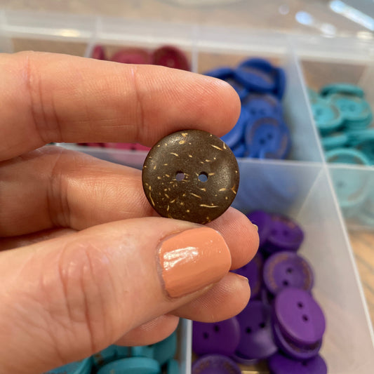 Brown button held by a hand with a background of colorful buttons.