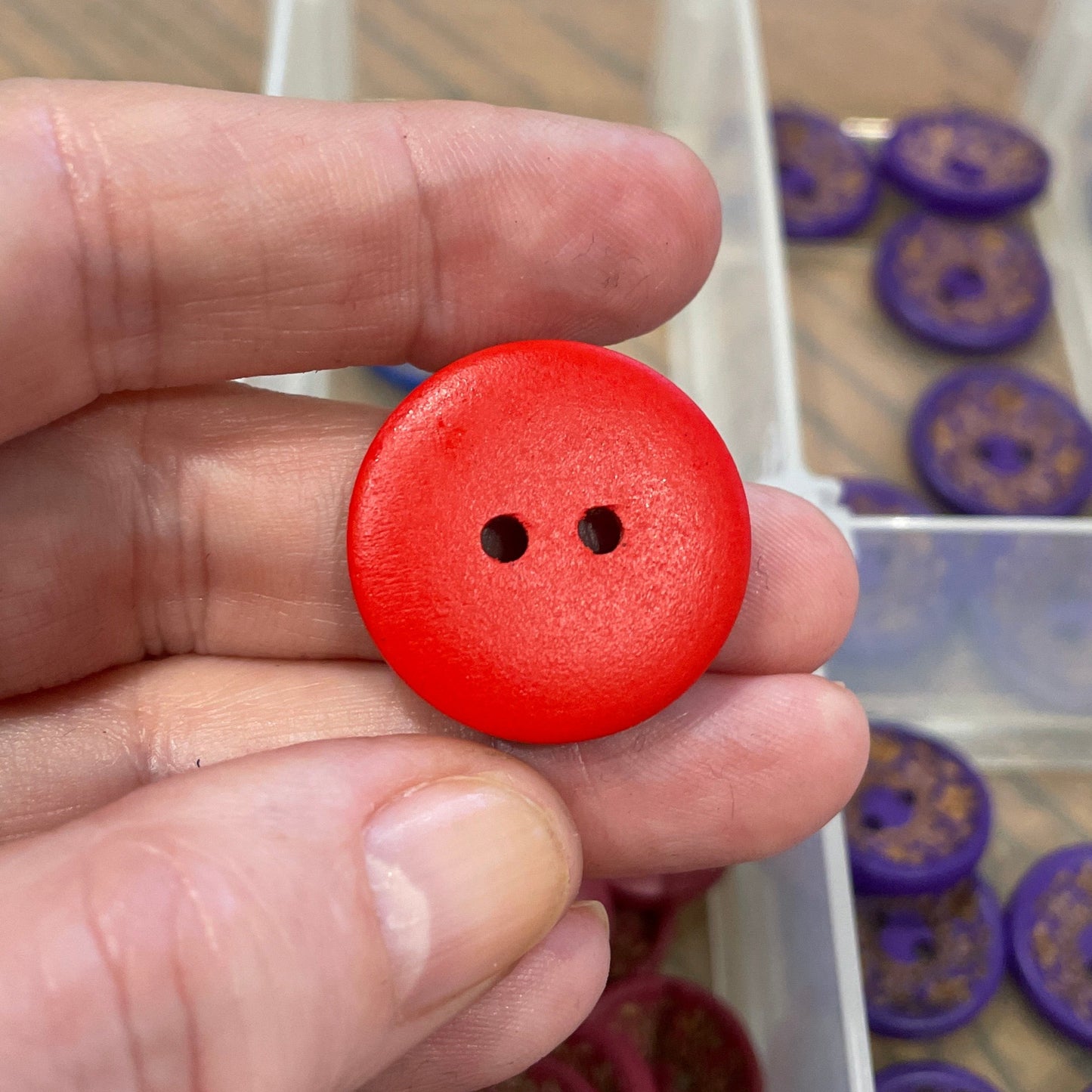 Red button held by a hand with a container of buttons in the background