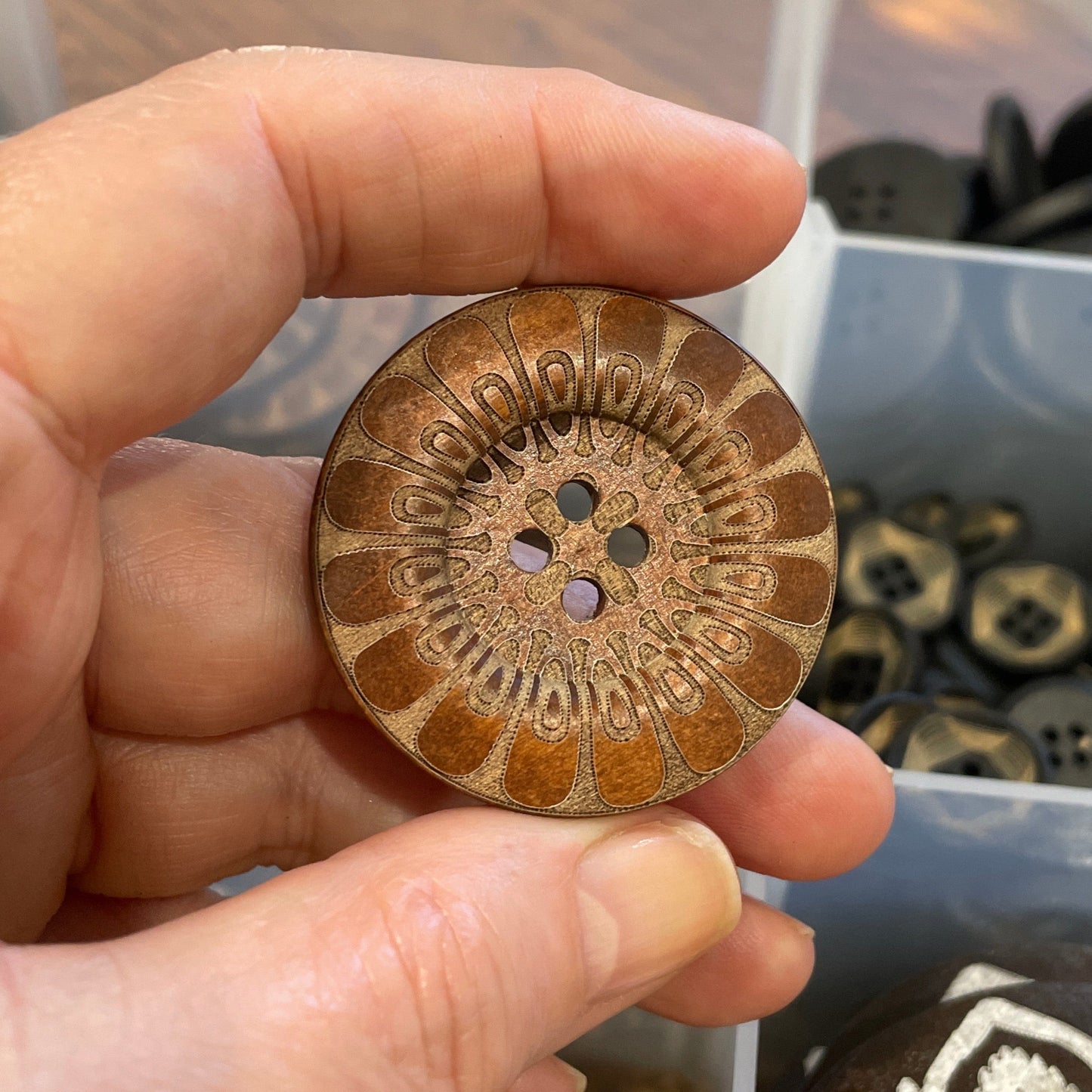 Hand holding a decorative button with a blurred background of button collection
