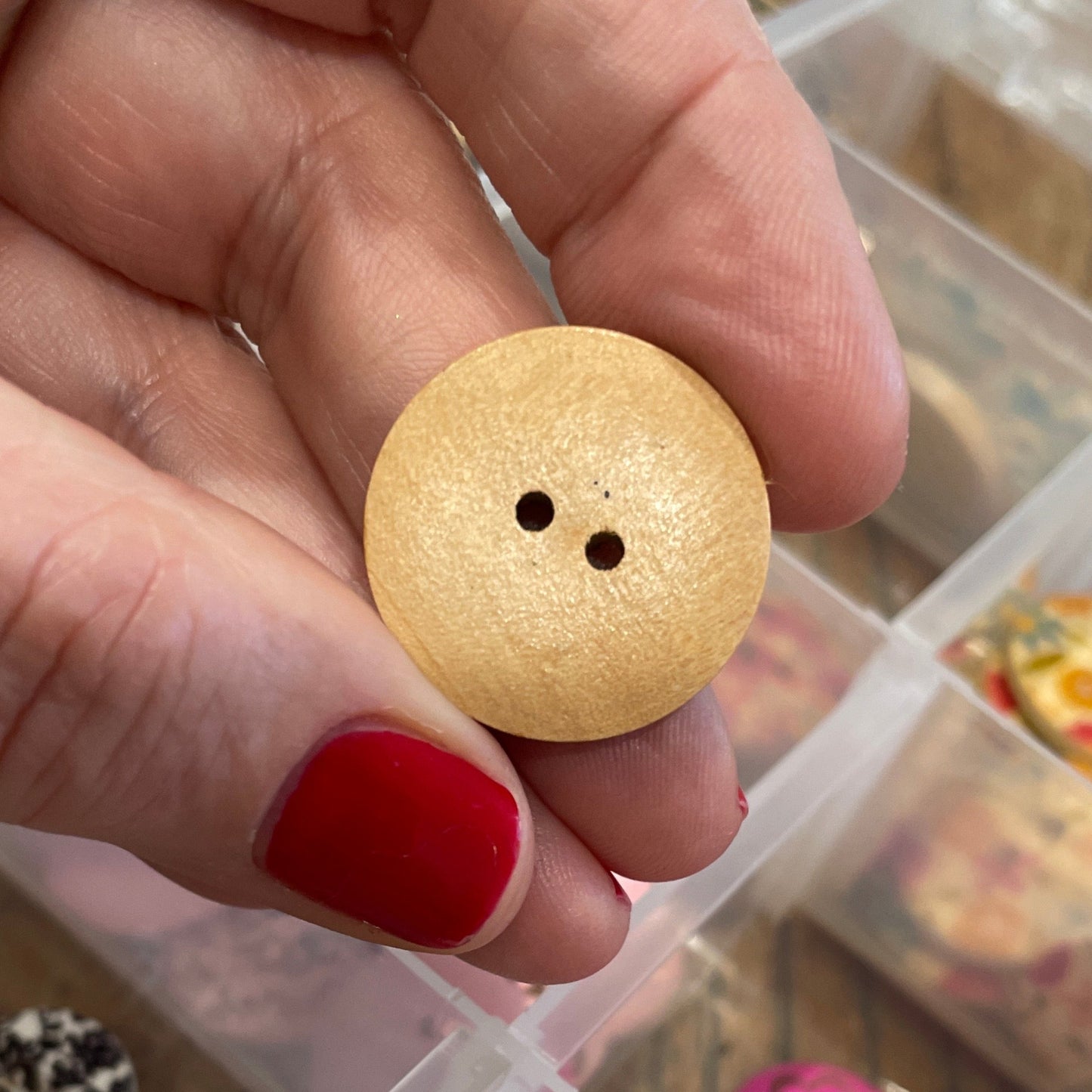 Hand holding a wooden button with a clear container of buttons in the background