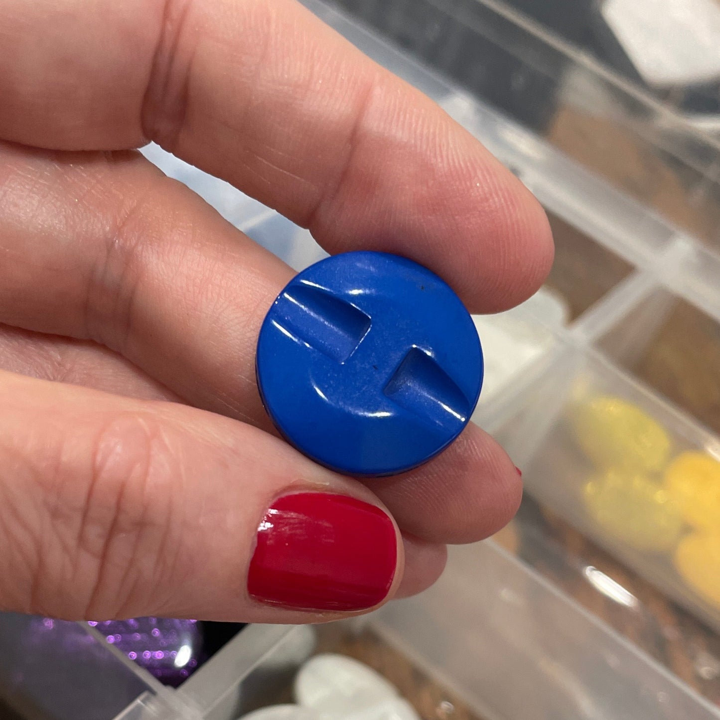 Hand holding a blue button with a container of various buttons in the background