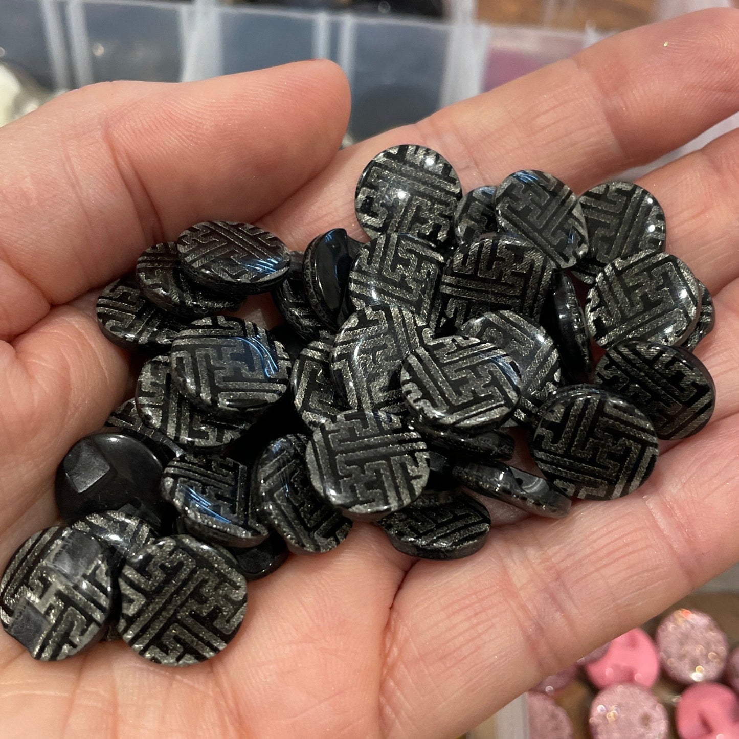 Hand holding black geometric beads with a blurred background of containers.