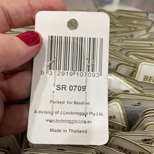 Barcode label held by a hand with red nail polish, against a background of similar labels.