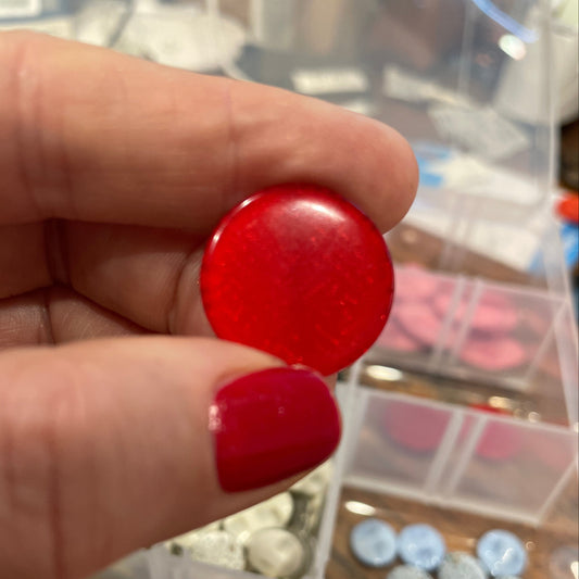 Red button held by a hand with a blurred background of a container with various buttons.
