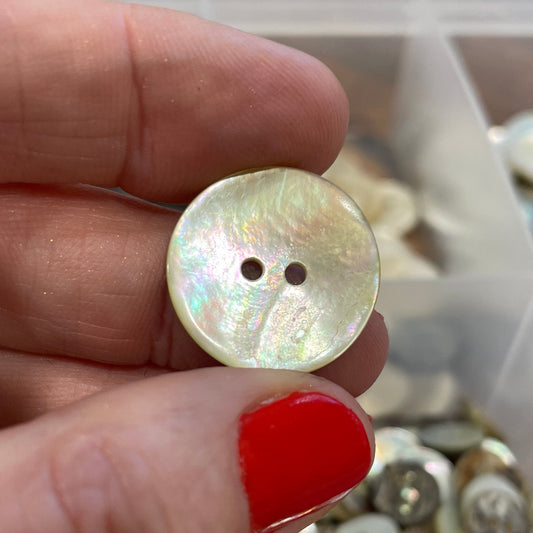 Hand holding a shell button with a container of buttons in the background