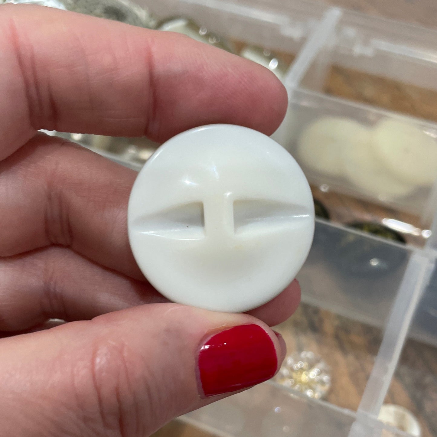 Hand holding a white button in front of a container with red and silver objects.