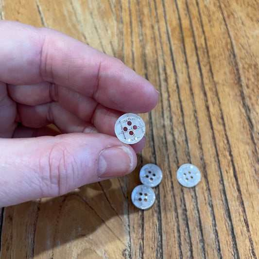 Hand holding a button with three additional buttons on a wooden surface