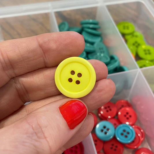 Hand holding a yellow button with a container of colorful buttons in the background