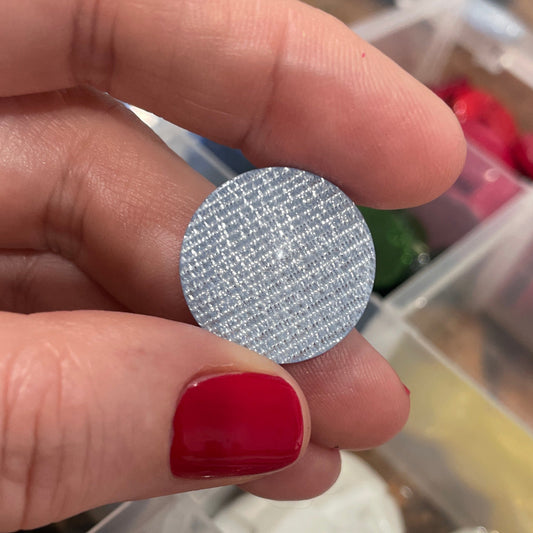 Hand holding a round, silver textured object with a blurred background of a jewelry box.