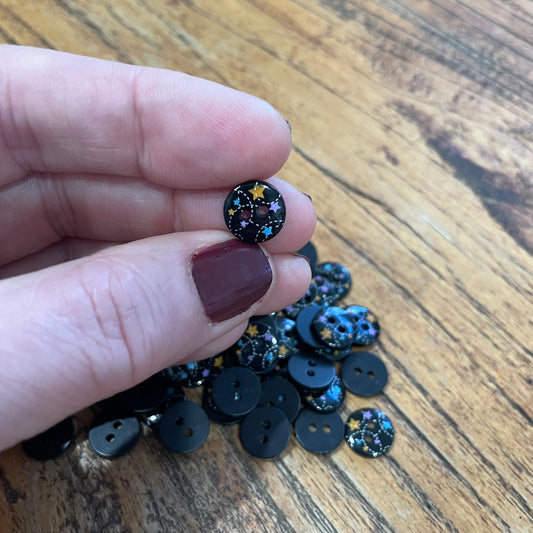 Black buttons with star designs held by a hand on a wooden surface