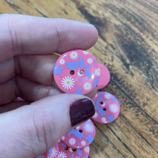 Hand holding a pink floral button with more buttons on a wooden surface