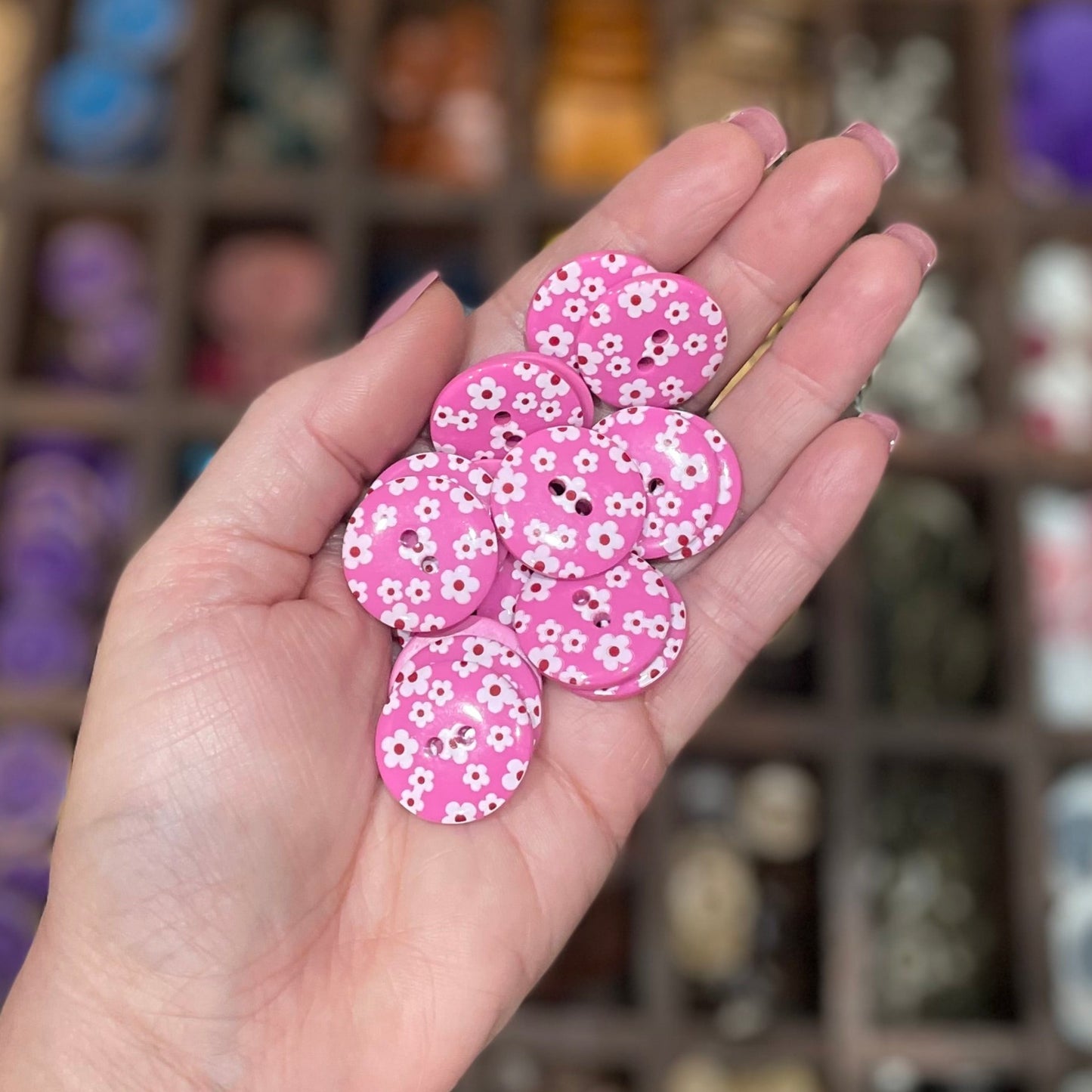 A hand holding several pink flower-shaped resin buttons with two holes each, displayed in a craft setting.