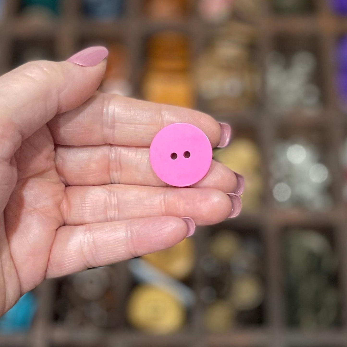 A hand holding several pink flower-shaped resin buttons with two holes each, displayed in a craft setting.