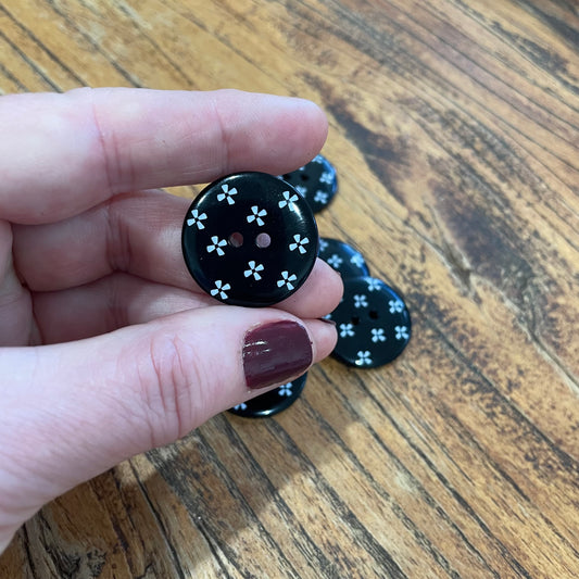 Black button with white floral pattern held by a hand on a wooden surface
