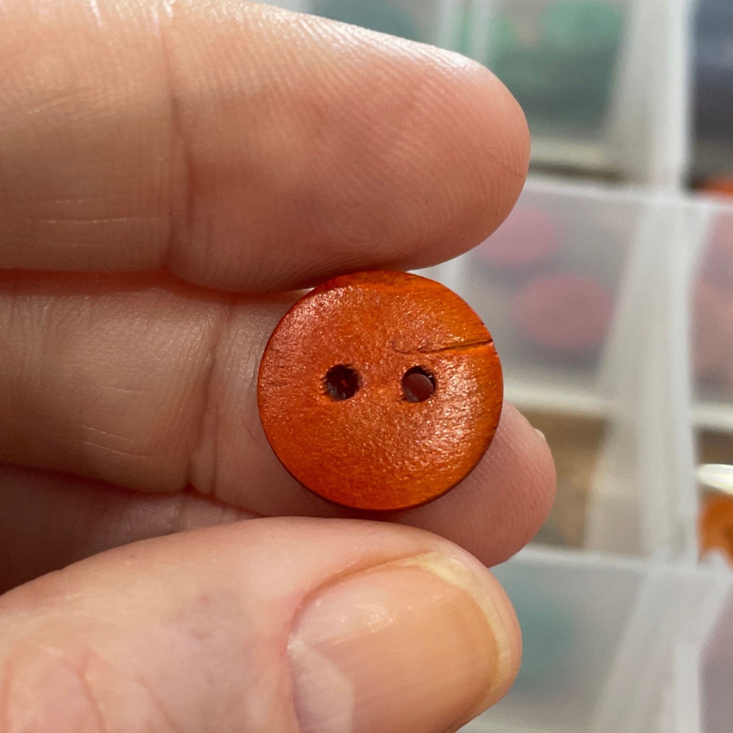 Hand holding a small orange button with a blurred background of a container with buttons.