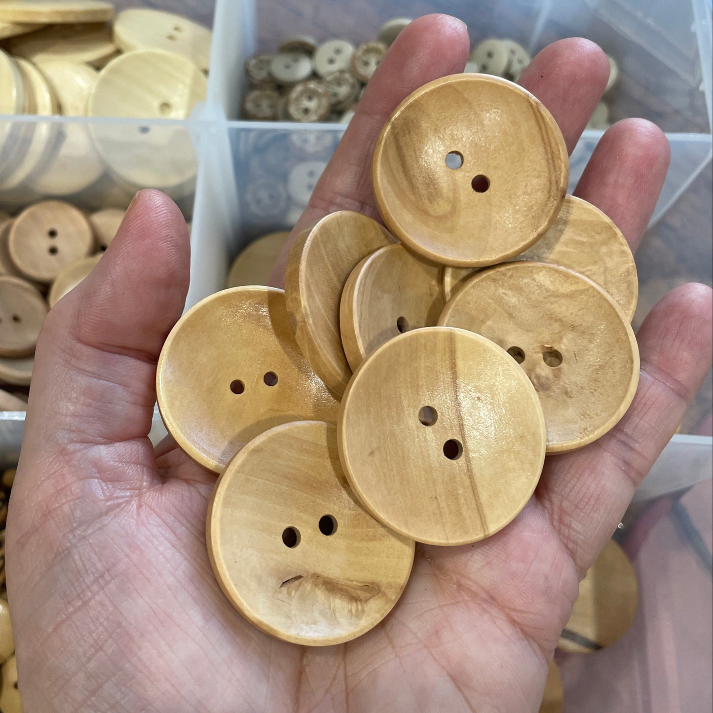 Hand holding wooden buttons with a clear container of buttons in the background