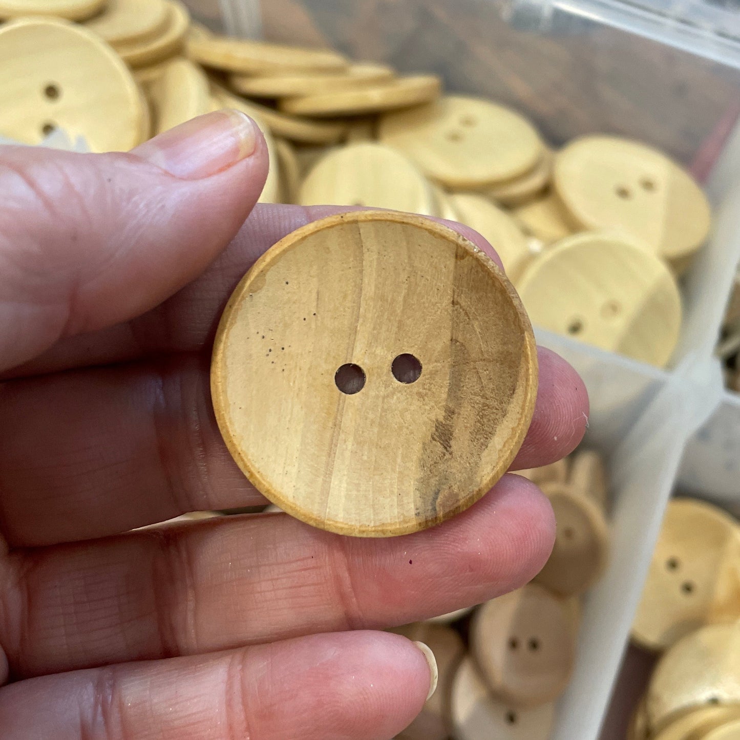Hand holding a wooden button with a container of buttons in the background