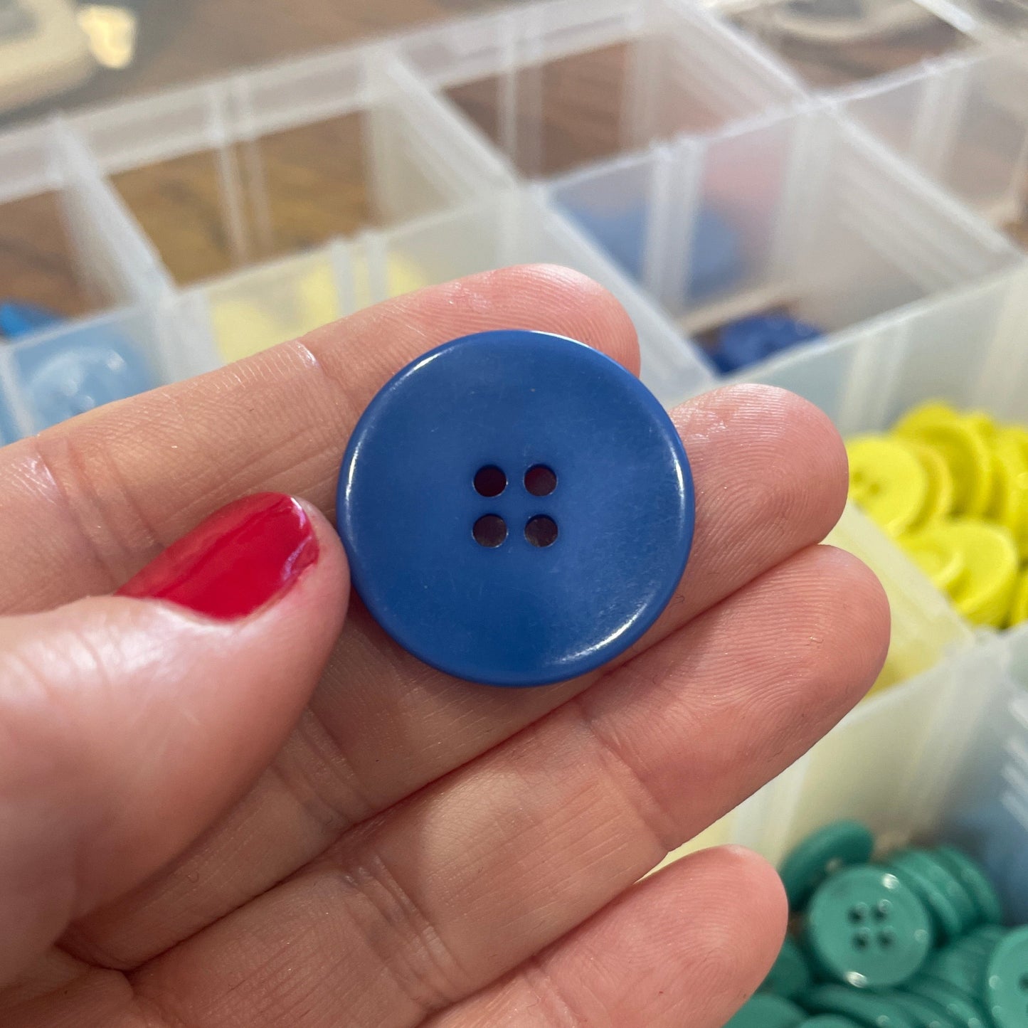 Blue button held in a hand with a container of buttons in the background