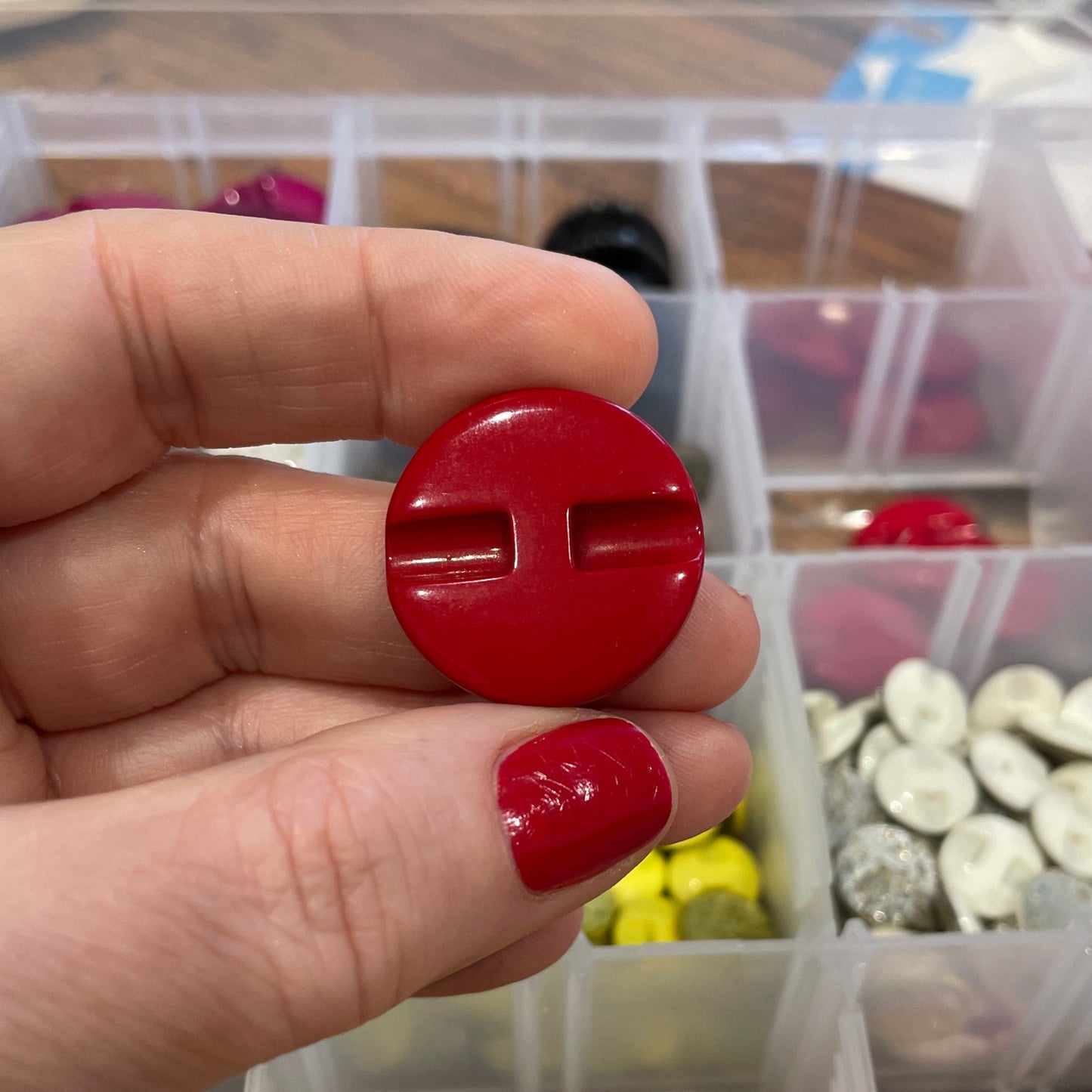 Hand holding a red button with a container of buttons in the background