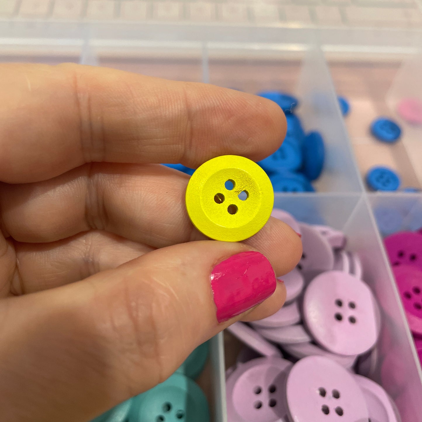 Hand holding a yellow button with a container of colorful buttons in the background