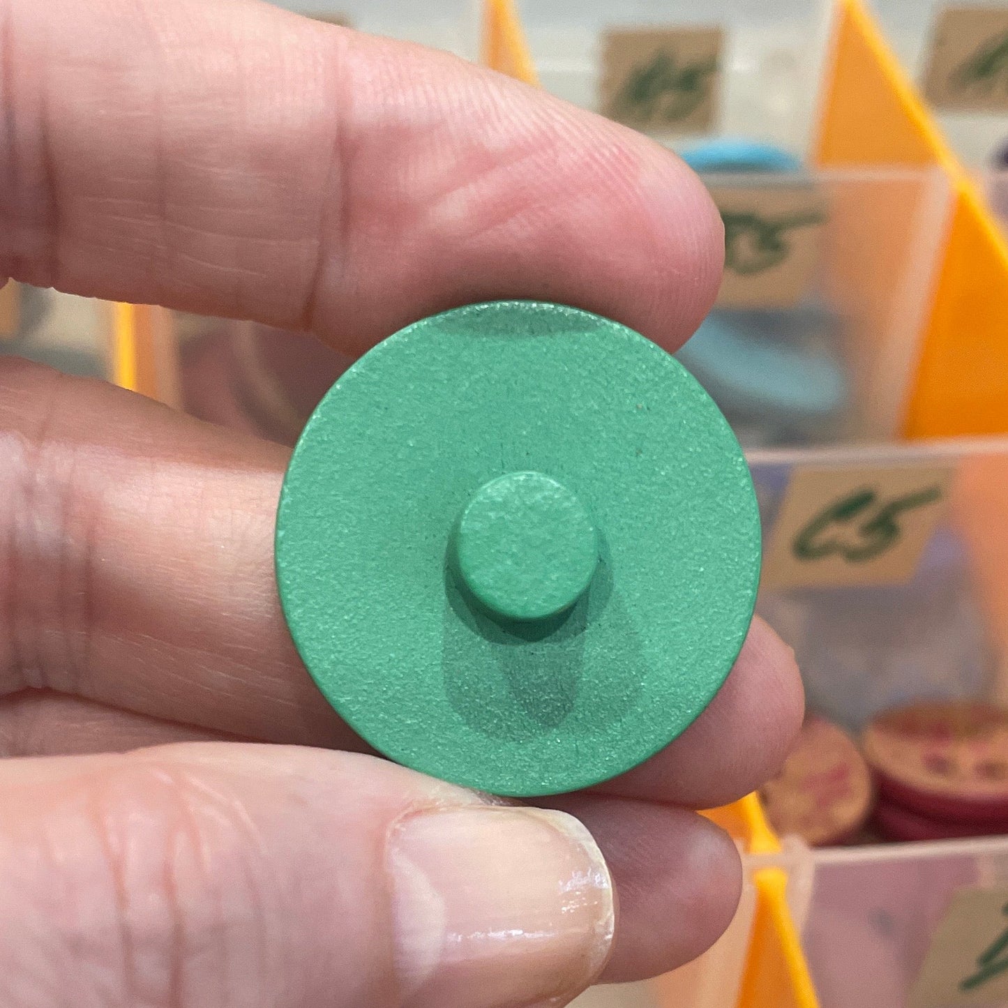 Green button held by a hand with a button organizer in the background
