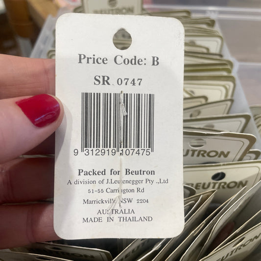 Close-up of a price tag with a barcode and text, held by a hand with red nail polish.