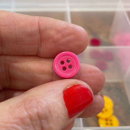 Pink button held between fingers with a container of buttons in the background