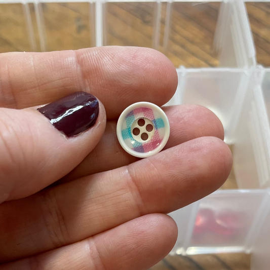 Hand holding a colorful button with a container of buttons in the background