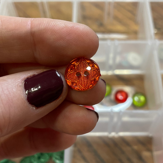 Hand holding a button with a container of assorted buttons in the background