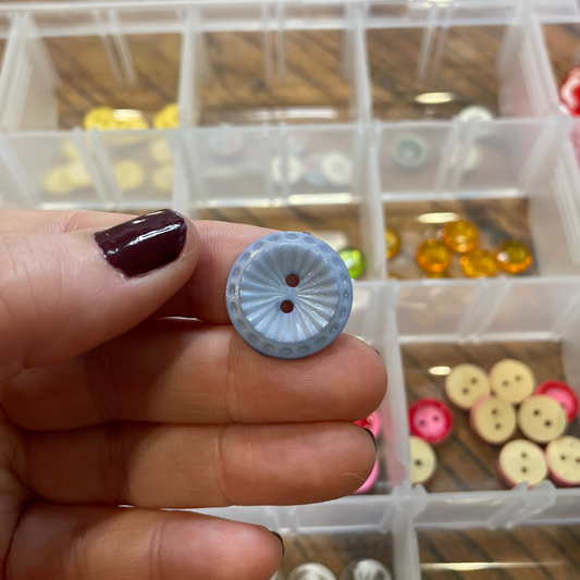Hand holding a small button with a clear container of buttons in the background