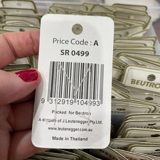 Hand holding a product tag with a barcode and text, with packaging of similar items in the background.