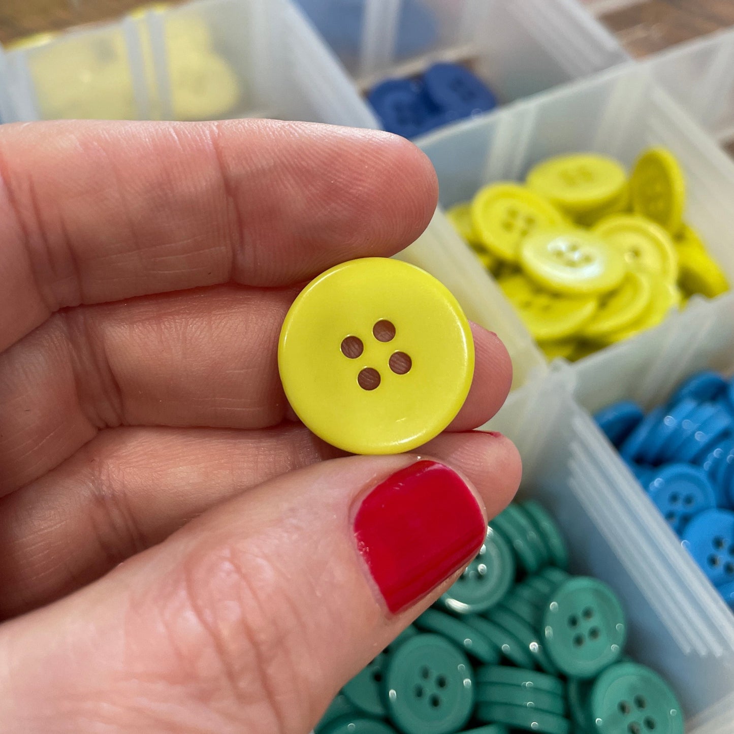 Hand holding a yellow button with a container of colorful buttons in the background