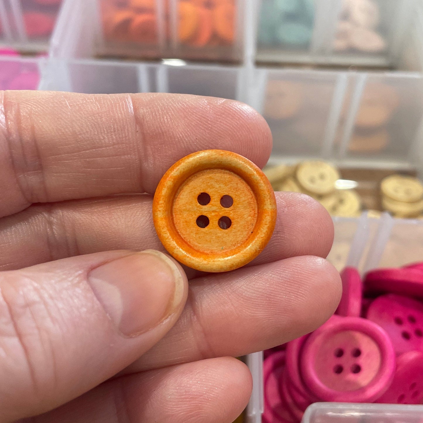 Hand holding a yellow button with a clear container of buttons in the background