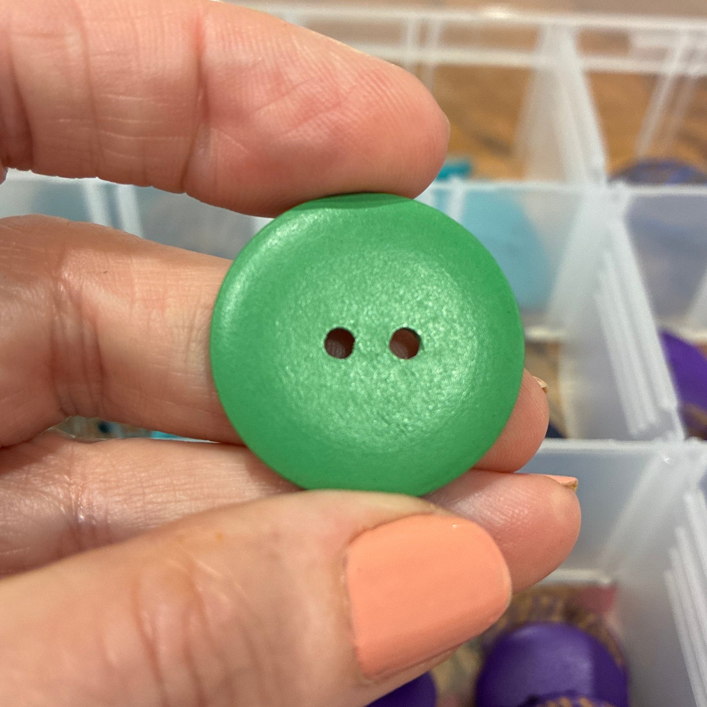 Green button held by a hand with a container of buttons in the background