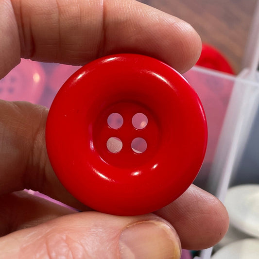 Hand holding a red button with a blurred background of buttons and containers