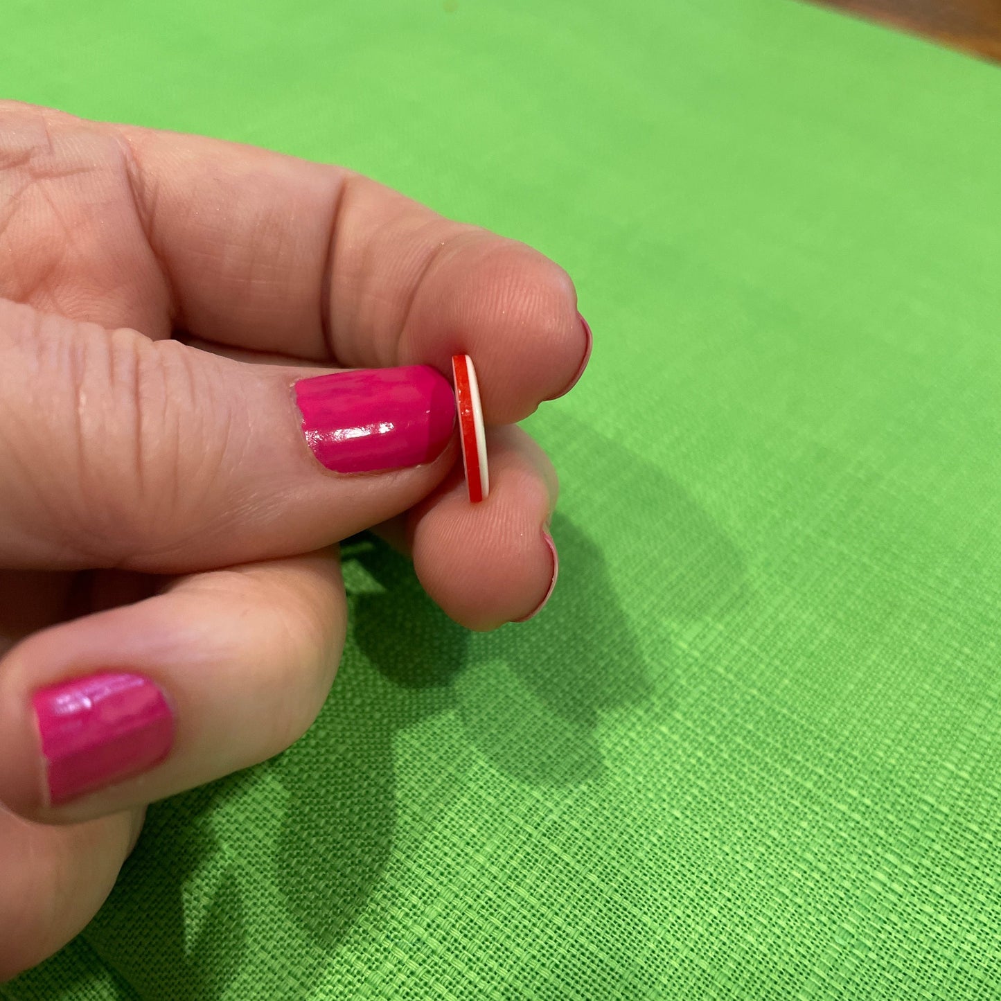 Hand with pink nail polish holding a small object against a green background