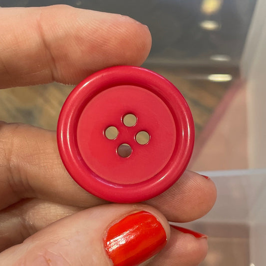 Hand holding a red button with a clear container of buttons in the background