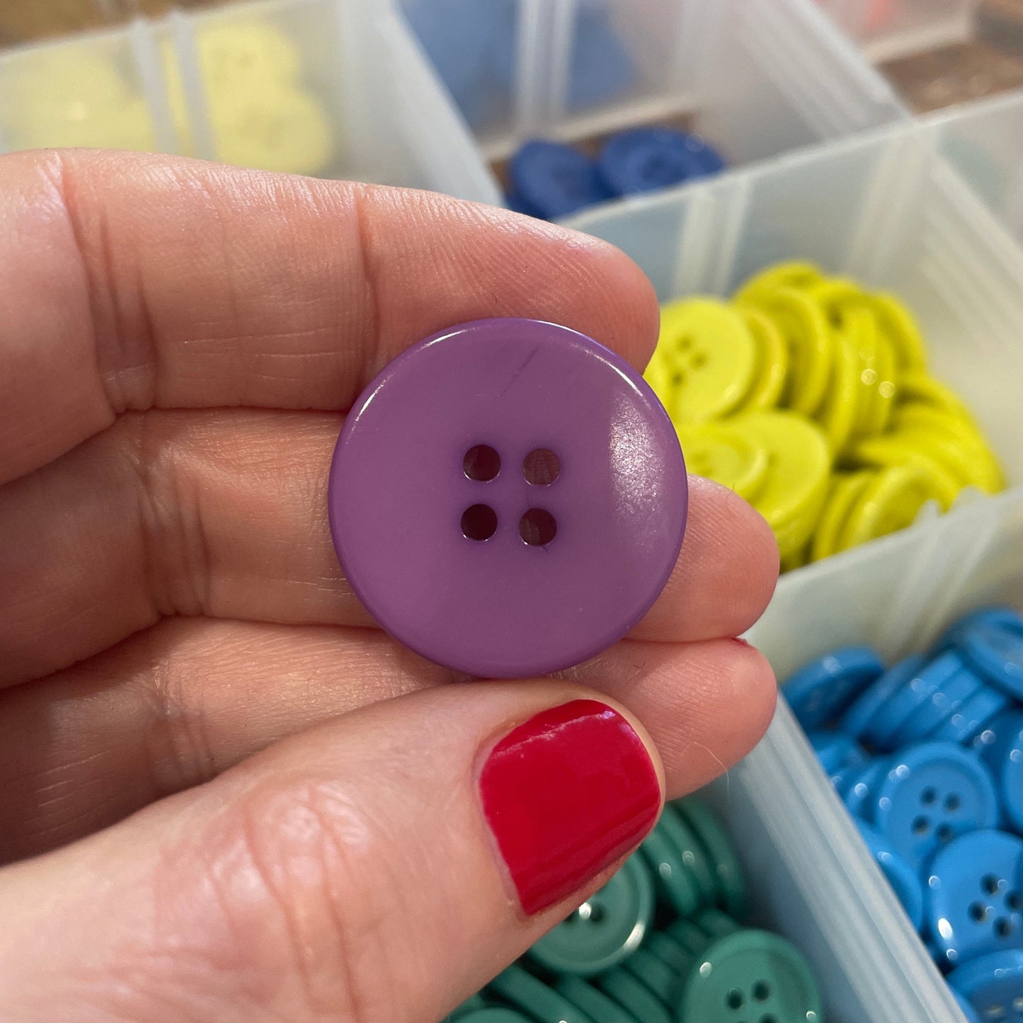 Hand holding a purple button with a container of colorful buttons in the background