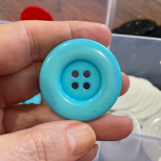 Hand holding a blue button with a blurred background of buttons and containers.