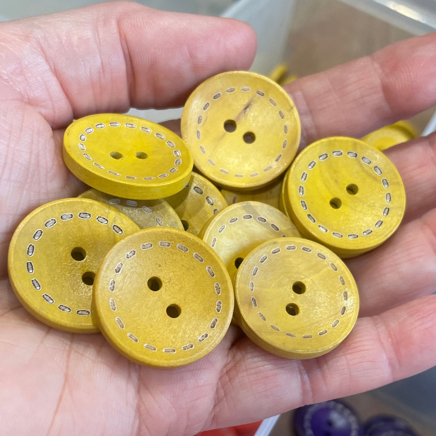Hand holding yellow buttons with a container of assorted buttons in the background