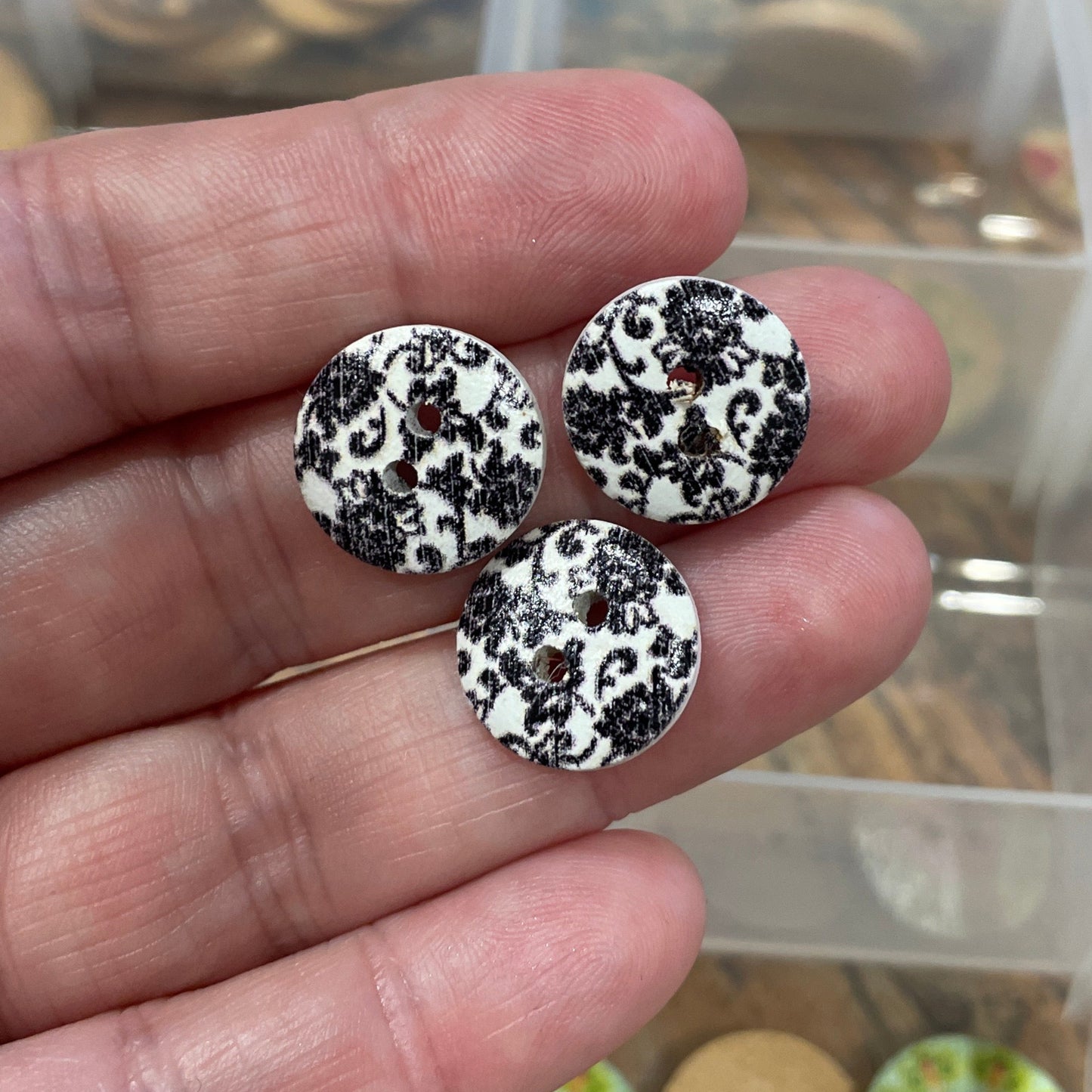 Hand holding three black and white patterned buttons with a container of buttons in the background.