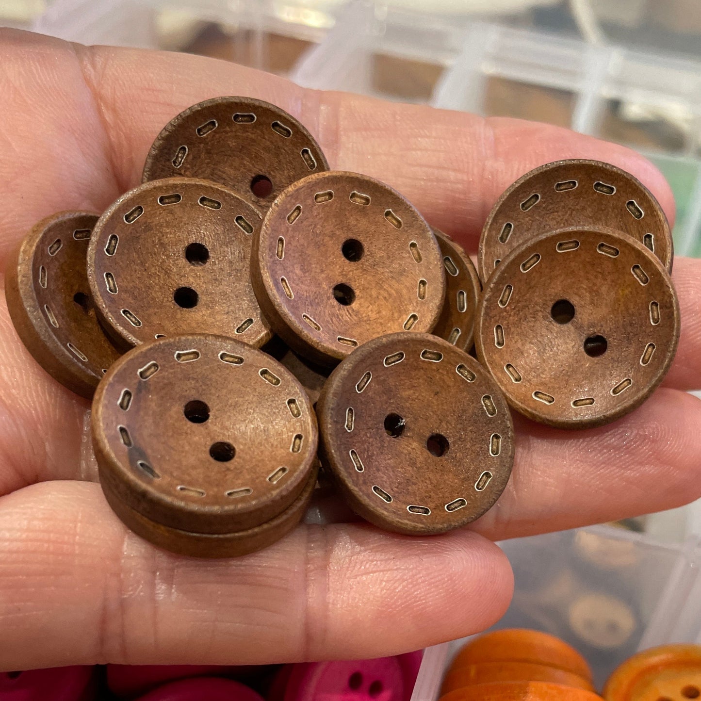 Hand holding brown buttons with a container of various colored buttons in the background.