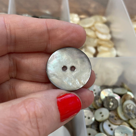 Hand holding a button with a container of buttons in the background