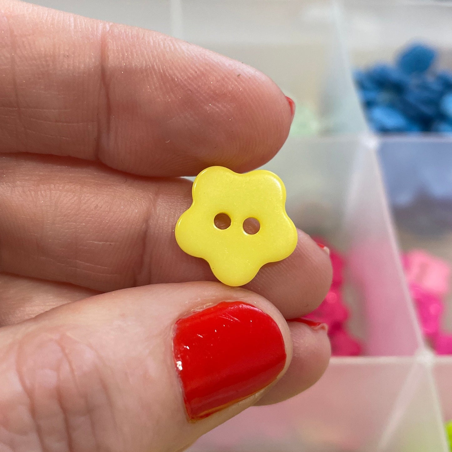 Hand holding a yellow flower-shaped button with a blurred background of more buttons.