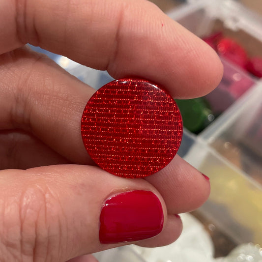 Hand holding a red textured round object with a blurred background of a storage box.