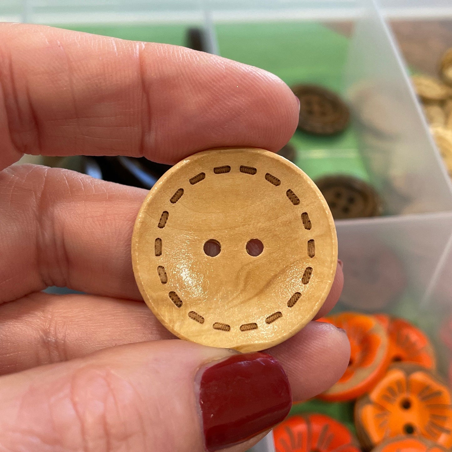 Hand holding a wooden button with a background of colorful buttons in a container.