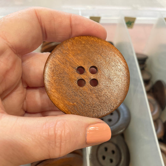 Hand holding a wooden button with a blurred background of more buttons.