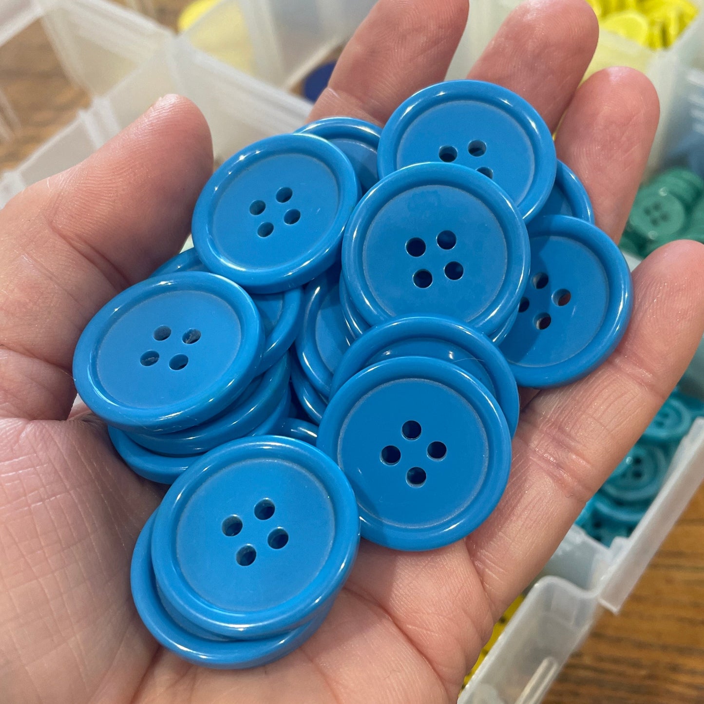 Hand holding blue buttons with a container of buttons in the background