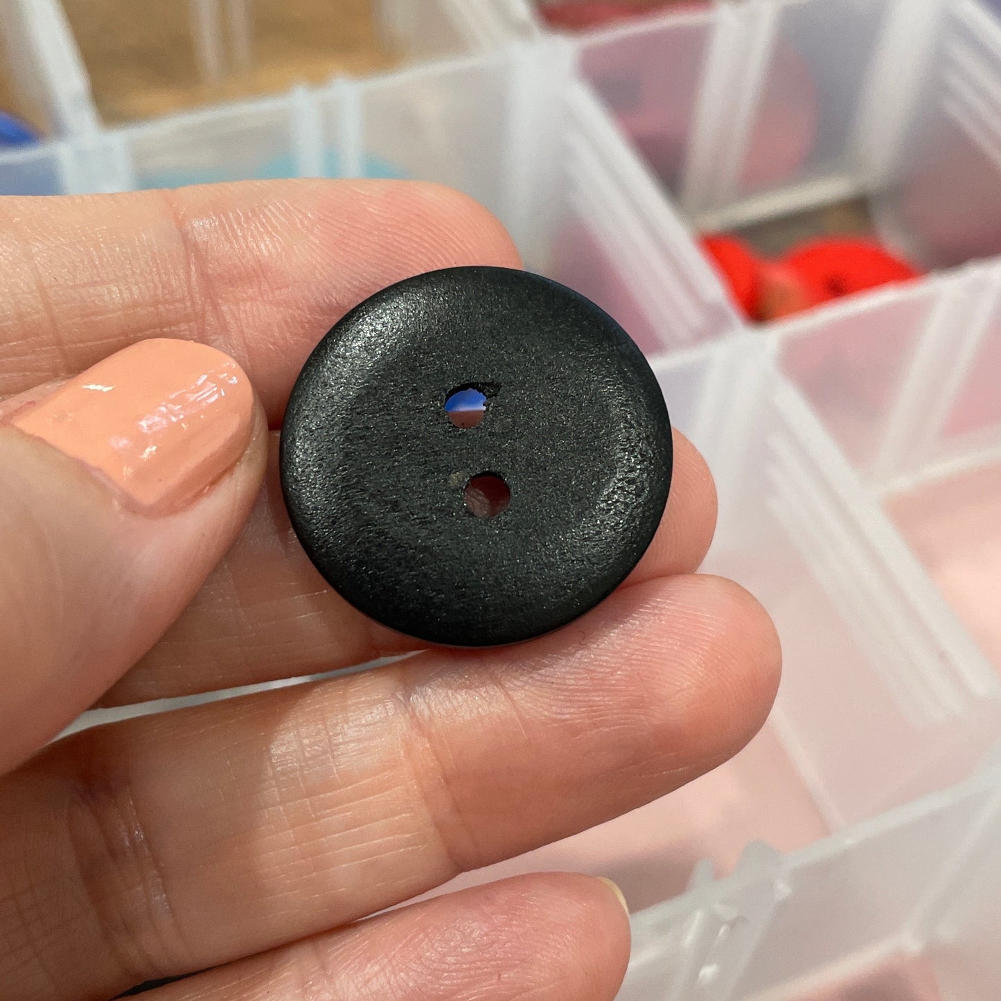 Black button held in a hand with a container of colorful buttons in the background