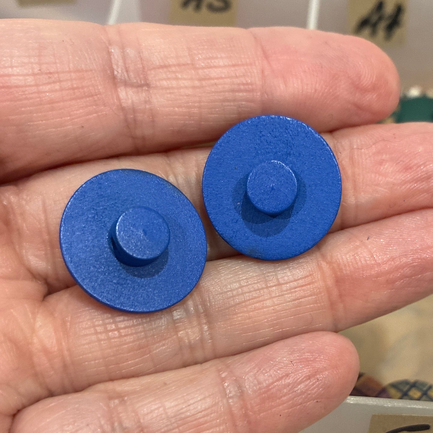 Hand holding two blue circular objects with a collection of buttons in the background.